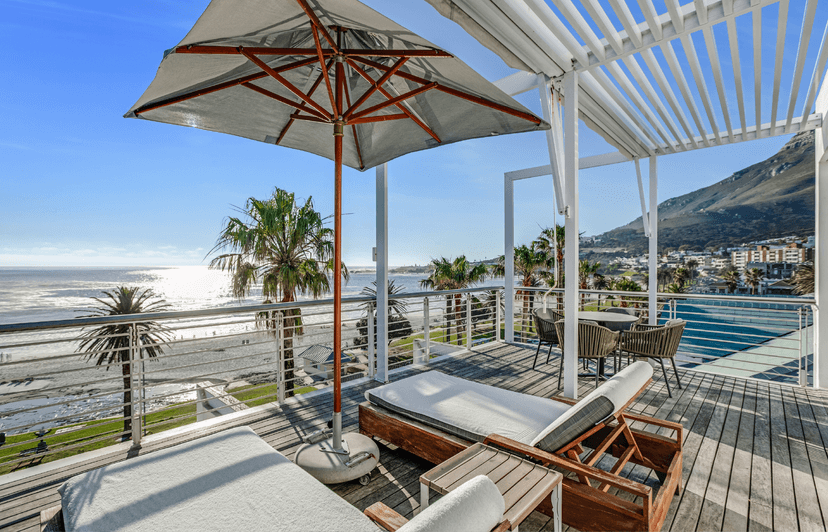 Junior Sea-Facing Suite balcony with sun loungers, umbrella and panoramic views of Camps Bay beach, palm trees and mountains