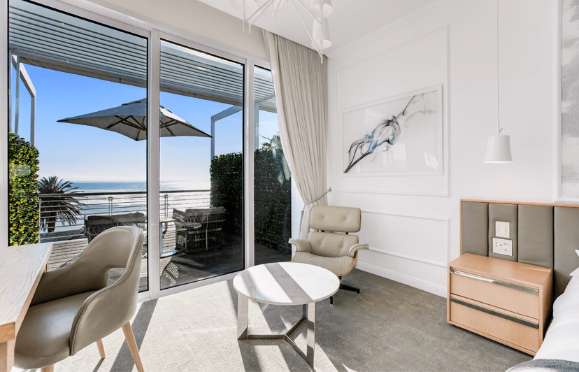 Studio Sea-Facing Room seating nook with Eames lounge chair, abstract art and sliding doors onto an ocean-view balcony