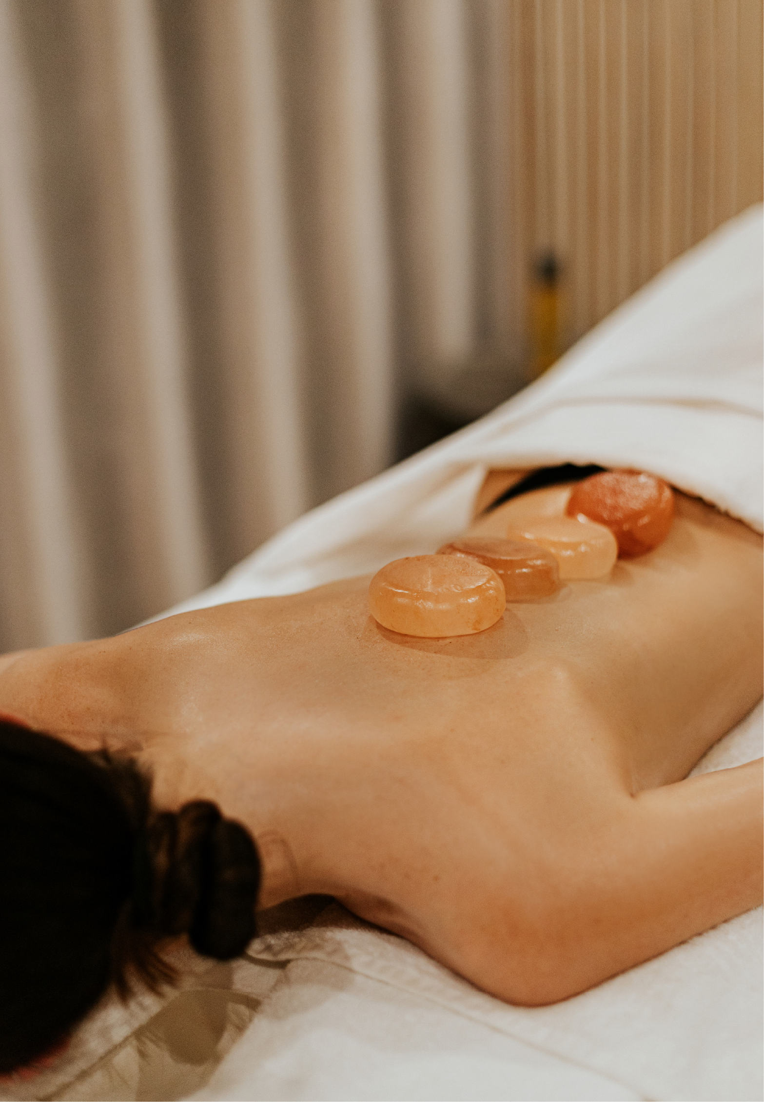 A spa guest lying face-down on a treatment table with a row of warm orange selenite stones placed along their spine during a hot stone massage treatment.