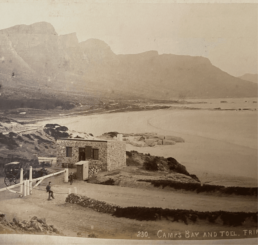 Sepia-toned historical photograph labelled 'Camps Bay and Toll' circa 1890, showing a stone toll house on a dirt road above a largely undeveloped beach, with the mountains visible in the distance.