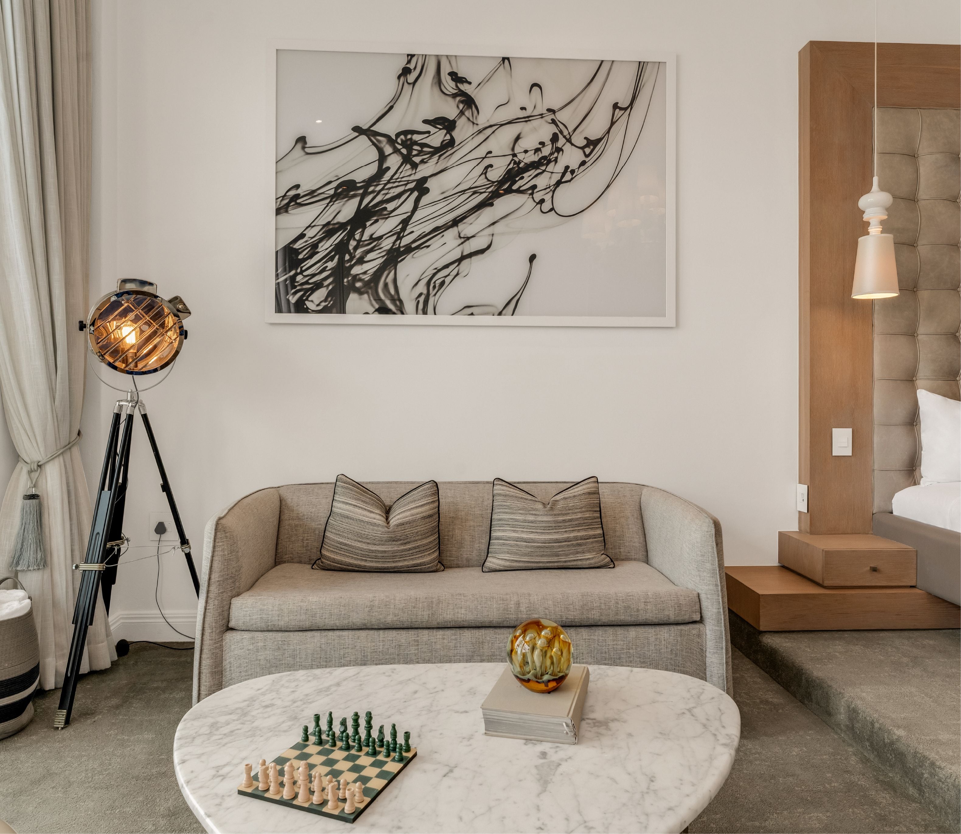 Seating nook in a Deluxe Sea-Facing Suite with tufted sofa, abstract artwork, tripod floor lamp and chess set on marble table